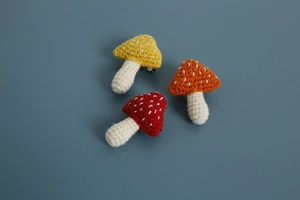 Close-up of three handmade crochet mushroom brooches in yellow orange and red colors