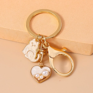 Detail of white enamel cat charm and pearl heart pendant on gold lobster clasp keychain