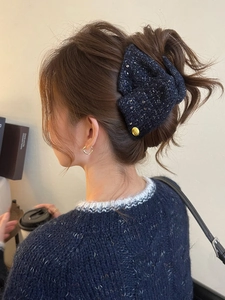 Detail view of navy blue tweed bow shark clip worn on a bun hairstyle with silver sequins
