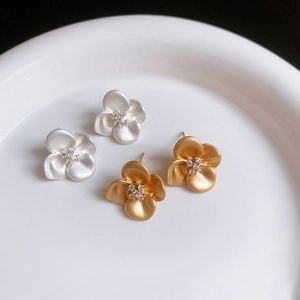 Detail view of pearl white and matte gold flower stud earrings with zircon center