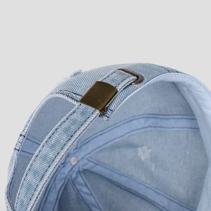Close-up of light blue denim cap showing adjustable metal buckle and distressed detail