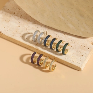 Detail shot of multicolor zircon-encrusted C-shaped ear cuffs on textured stone surface