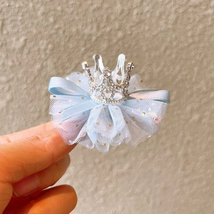 Handheld view of a silver rhinestone crown hair clip with a light blue tulle bow