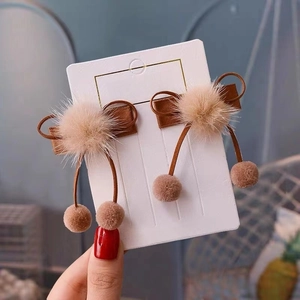 Close-up of brown bow hair clips with plush pom-poms for girls on white card