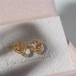 Detailed close-up of gold smiley face stud earrings with beaded texture on jewelry box