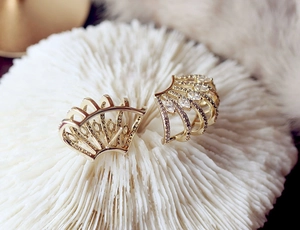 Macro shot of gold-plated arc earrings with sparkling zircon stones on white coral base