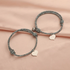 Magnetic heart pendant bracelets in grey-blue woven cord for couples on silk background