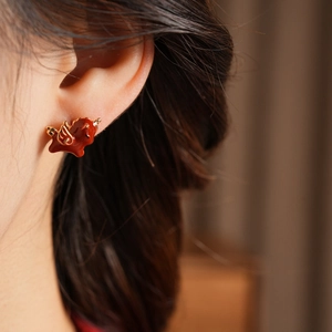 Detailed close-up of 18k gold-plated red pony earrings with enamel on a model's ear