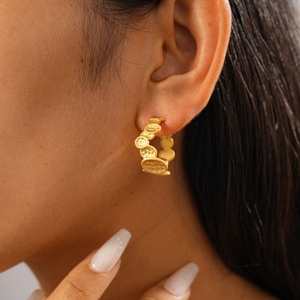 Close-up of model wearing gold hoop earrings with irregular hammered texture plates