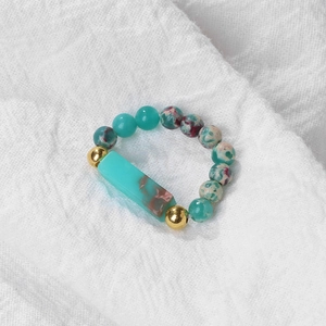 Macro shot of 4mm bloodstone beaded ring with turquoise accent on white linen fabric