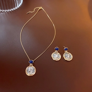 Detail view of retro coin earrings and necklace set with blue gemstone in gold and silver