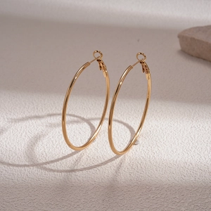 Minimalist metallic gold hoop earrings with polished finish on a textured surface