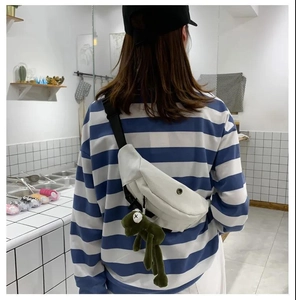 Rear view of a white canvas chest bag with a green frog plush pendant on a model