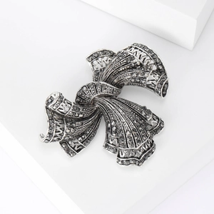 Detail of silver vintage bow brooch with micro-paved black rhinestones on a white surface