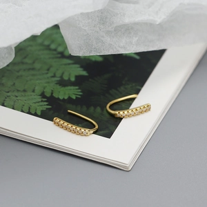 Macro detail of elegant gold-plated curved zircon ear hooks on decorative paper background