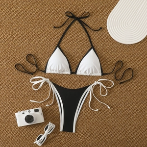 Flat lay of black and white bikini set with cross ties on a woven straw mat background