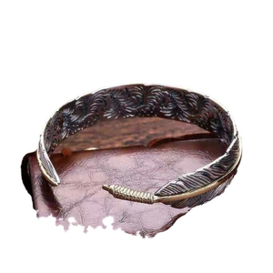 Vintage alloy feather open bracelet in bronze and silver finishes on leather background