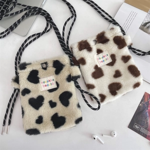 Close-up of heart pattern plush crossbody bags with strap on a minimal white desk