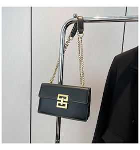 Detail of black rectangular crossbody bag featuring a golden geometric clasp and chain strap