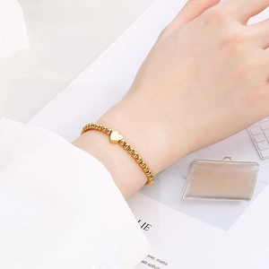 Close-up view of a minimalist gold heart charm beaded bracelet on a female wrist