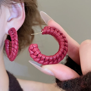 Close-up of red leather woven C-shaped hoop earrings with gold posts and texture