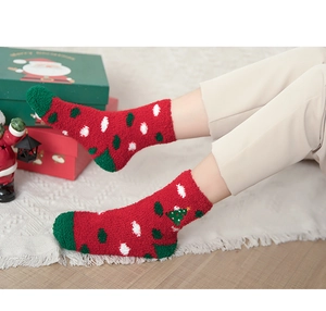Detail of soft red Christmas coral fleece socks with green tree pattern on carpet