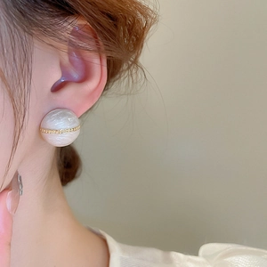 Close-up of pearl-white round stud earring with gold chain inlay worn by a model