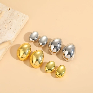 Close-up of sleek gold and silver oval hoop earrings in various sizes on a beige backdrop