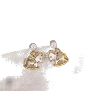 Golden rocking horse earrings with pearls and crystals on a soft grey textile background