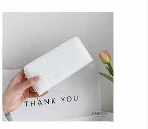 Detail of white pebble grain leather long wallet with golden zipper held against tulip