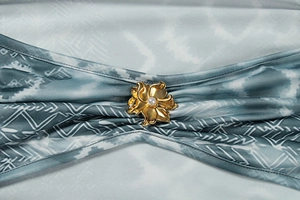 Detailed view of an artistic golden flower brooch with a white pearl on printed fabric