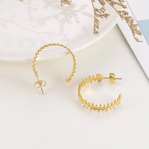 Detail of golden fishbone C-shaped hoop earrings with textured metal finish