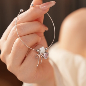 Detail of silver bangle with purple heart gemstone, star charm, and bow knot pendant