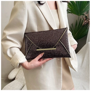 Détail de pochette enveloppe à paillettes avec bordure dorée en V sur tenue de blazer blanc