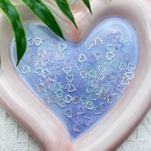 Iridescent hollow heart nail art sequins in a ceramic dish with soft gradient colors