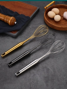 Three-piece stainless steel whisk set in gold, black, and silver on a rustic kitchen counter