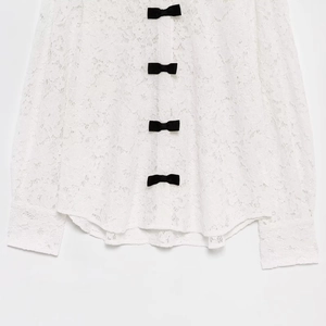 Elegant white lace long sleeve top with contrasting black bows on a clean background