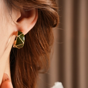 Close-up of vintage C-shape gold earrings with dark green enamel on a model ear