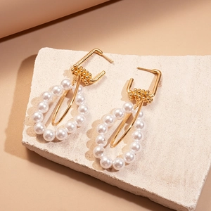 Elegant gold geometric earrings with teardrop pearls on a stone base display