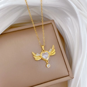 Macro shot of gold heart pendant with wings and sparkling crystals on beige jewelry box