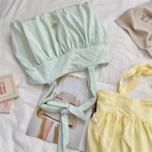 Detail of ruffled canvas tote bags in green and yellow with adjustable bow tie straps
