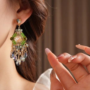 Detail of bohemian gold earrings featuring green rhombic stones and beaded fringes on model
