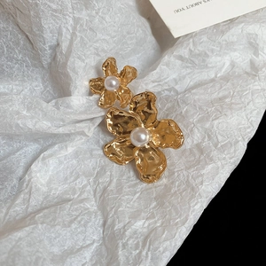 Detailed close-up of golden flower stud earrings with central white pearls and hammered texture