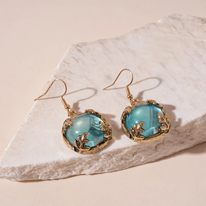Detail of vintage gold earrings with teal resin stones on a textured stone surface