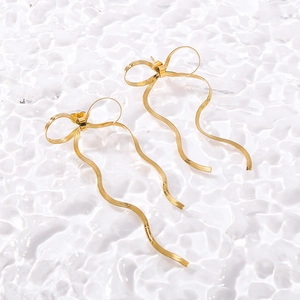 Detail of gold bow earrings with wavy metal tassels on a rippled water background