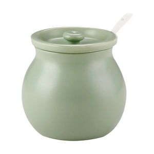Green ceramic seasoning jar with lid and white spoon on white background