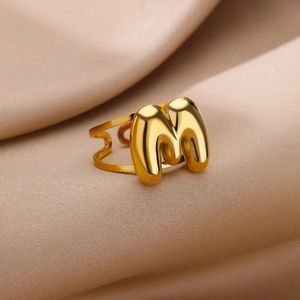 Macro shot of bubble style letter M gold ring detail on beige satin fabric background