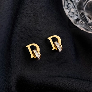 Elegante goldene Buchstaben-D-Ohrringe mit Zirkonia auf schwarzem Satin-Hintergrund