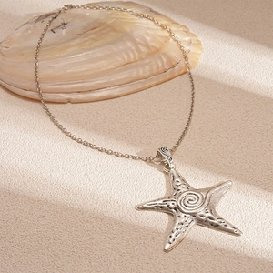 Macro shot of vintage silver starfish pendant on textured sand background with sea shells