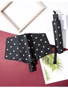 Flat lay of black polka dot folding umbrella with matching pouch on artistic background
